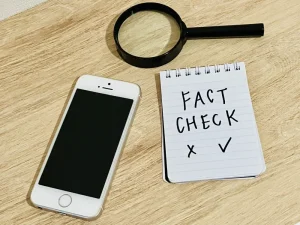 「FACT CHECK」とメモ書きされたノートとスマートフォン、虫眼鏡