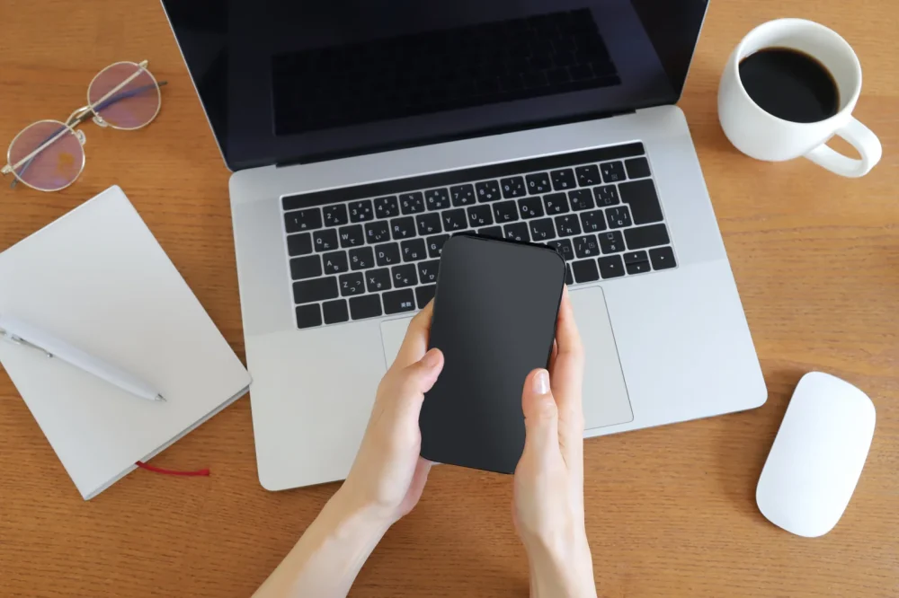 ノートパソコンとスマートフォンを操作する手元とデスク