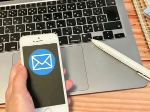 メール通知アイコンが表示されたスマートフォンを持つ手とノートパソコンのキーボード