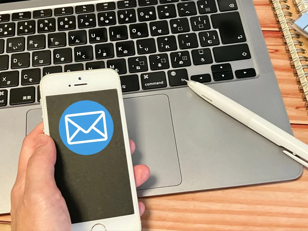 メール通知アイコンが表示されたスマートフォンを持つ手とノートパソコンのキーボード