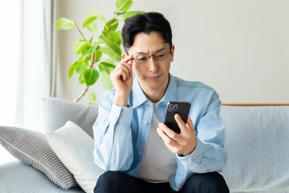 スマートフォンの画面を見て考え込む男性