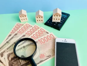 1万円札とミニチュアの家、虫眼鏡とスマートフォン